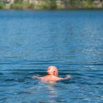 man-swimming-in-a-blue-lake-with-trees-9t9tavlbbj8